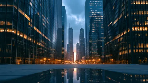 A canyon of tall glass towers at dusk, with warm lights reflected in a still plaza.