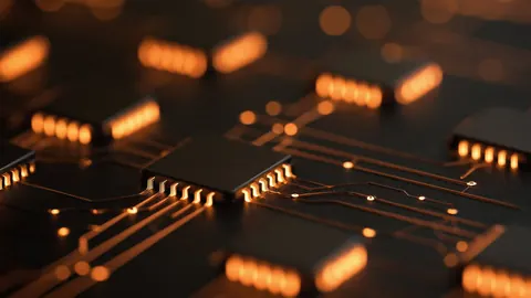Microchips on a dark circuit board, lit by warm amber light along their pins.