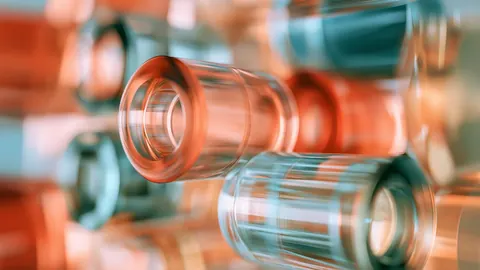 Clear glass cylinders and lenses stack at angles, catching warm copper and cool teal reflections.