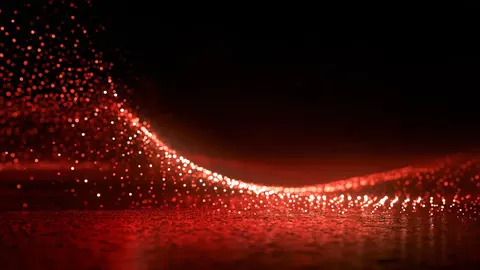 Millions of tiny red sparks gather into a curving tide that glitters against black.