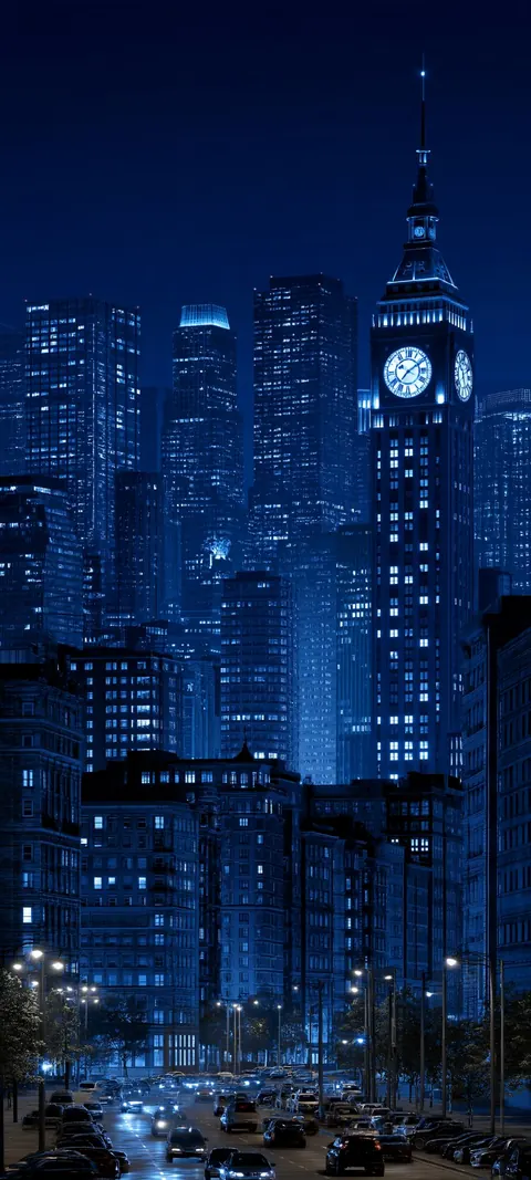 A blue city at night, with a lit clock tower rising above office towers and a busy street.